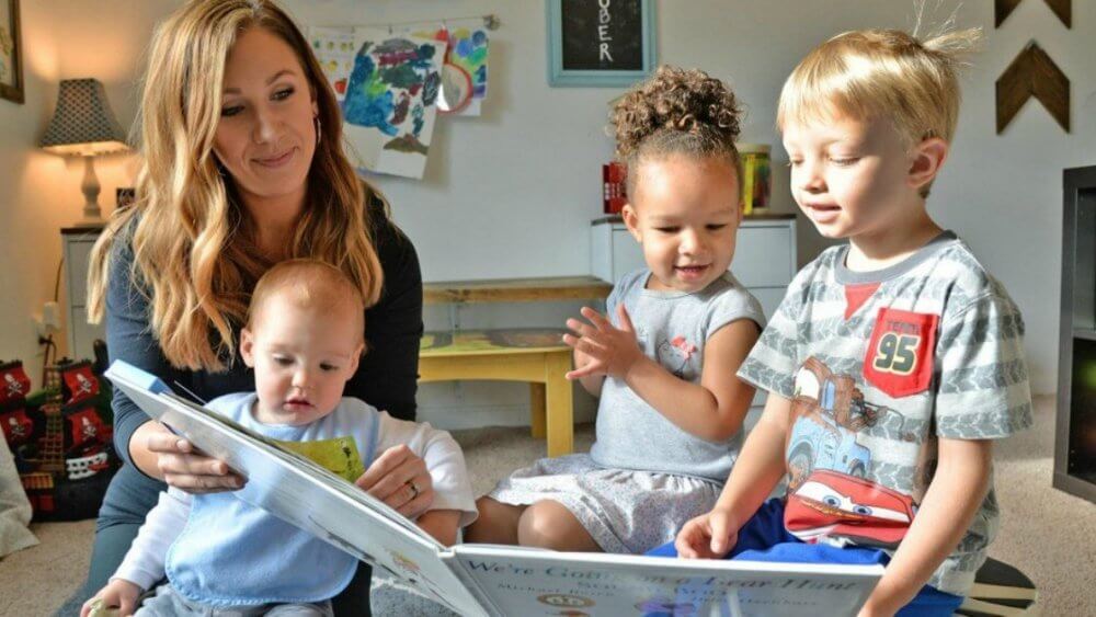 Childcare professional reading a book to three kids