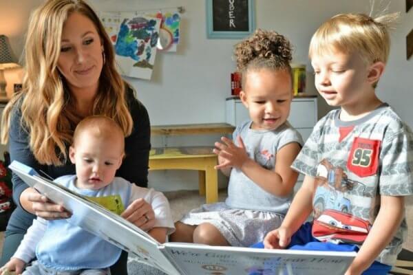 Childcare professional reading a book to three kids