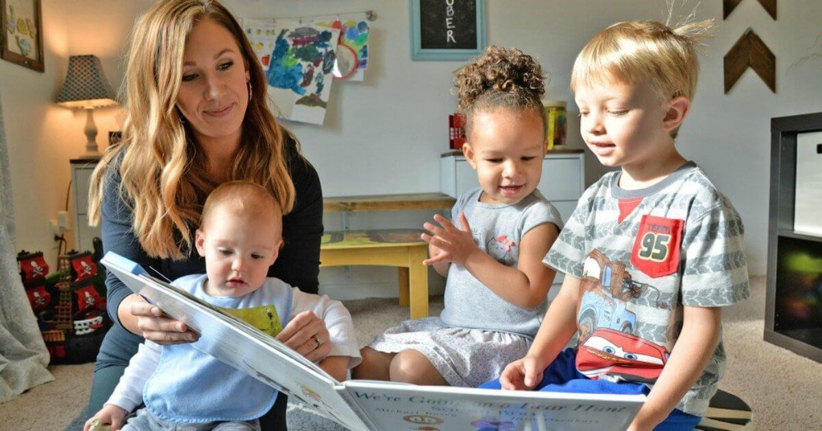 Childcare professional reading a book to three kids